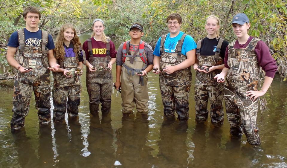 Seven students in waders holding fishing supplies