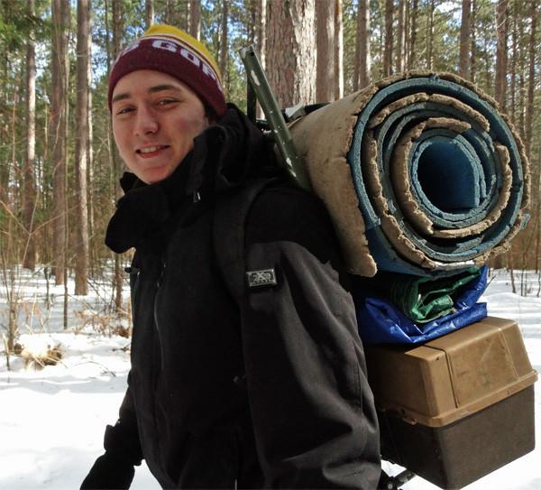 A student outside in the winter with a lot of supplies carried on his back